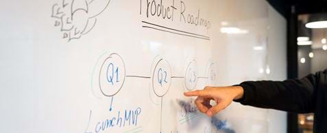 Post-it notes stuck on a glass wall, with the focus blurring into the background with the words: Product Road map above the notes.