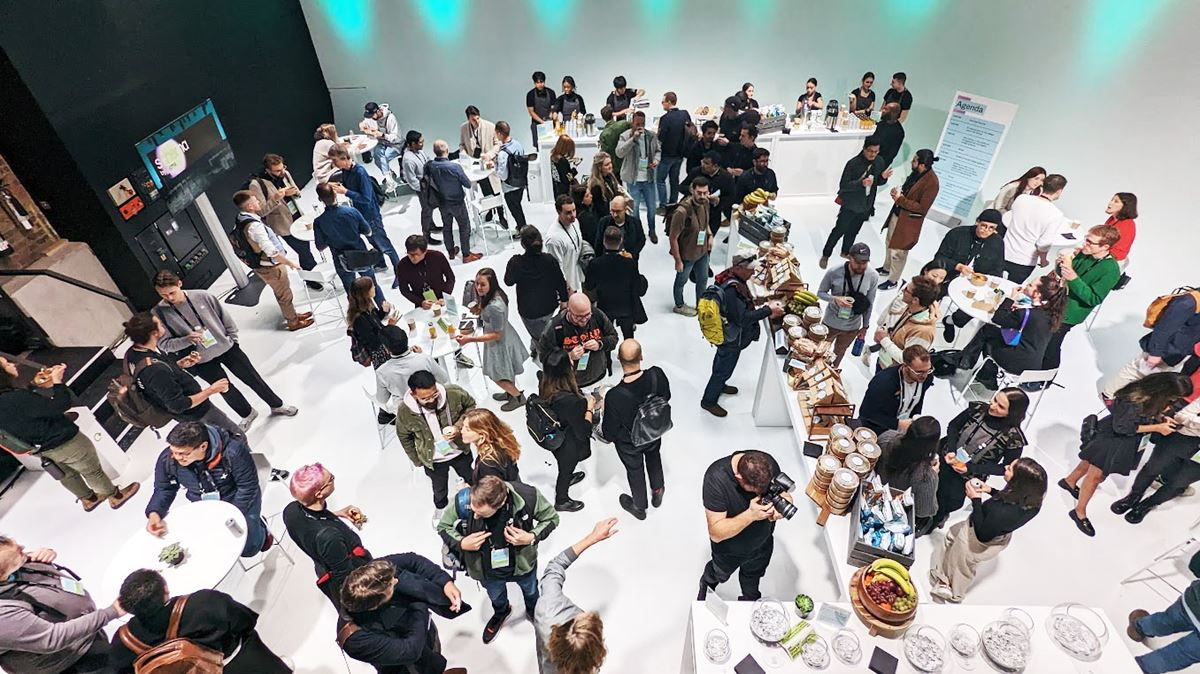 A group of people standing. Some of them are talking and holding plates and some are at a buffet table.