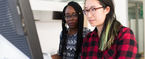 Two people stand together looking at a computer screen
