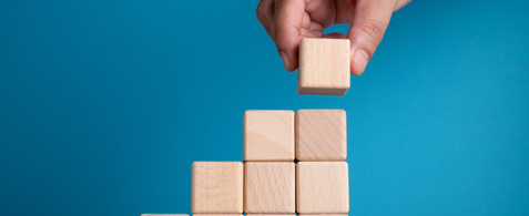 A hand placing a block atop a pile of wooden building blocks