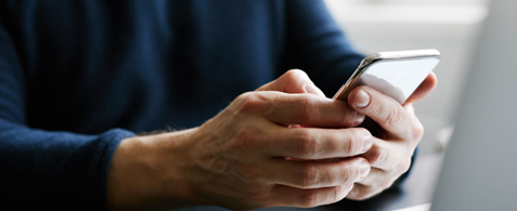 A pair of hands holding a mobile phone next to an open laptop.
