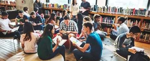 Students sat on casual seating in a library with rows of books in the background