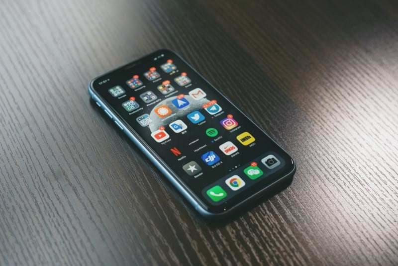 Phone lying on a table showing the home screen with lots of apps with notifications
