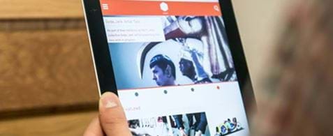 A tablet held up against a wooden wall, with the FACT website displaying on the screen.