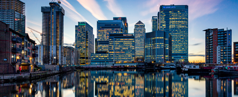 London's Canary Wharf skyline at dusk, with the buildings lit up against a purple sky.
