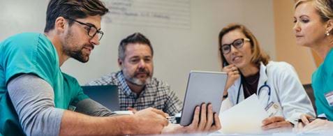 A group of doctors sat round a table looking at a tablet device