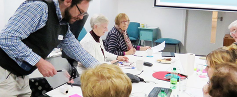 Justin from the Nexer team looks are post it notes on a table. Seated around him are several older people