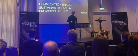 A speaker onstage at the Nexer sustainability summit in Malmo. A slide onscreen reads "How can tech enable sustainability and a promising future?"
