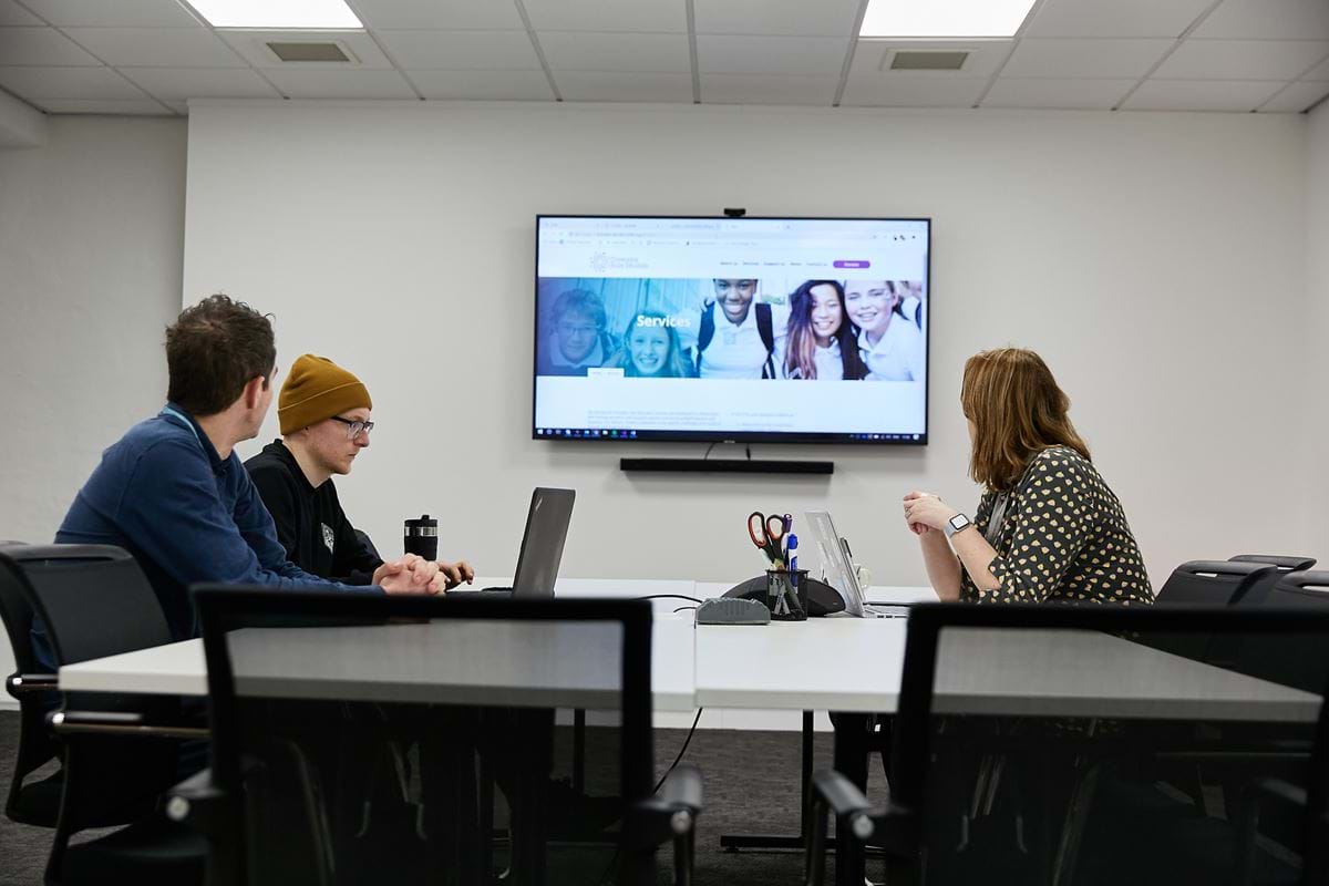 Three colleagues looking at a website image on a large screen discussing new requirements