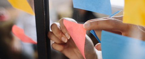 A hand sticks a post it note to a piece of glass which already features post it notes
