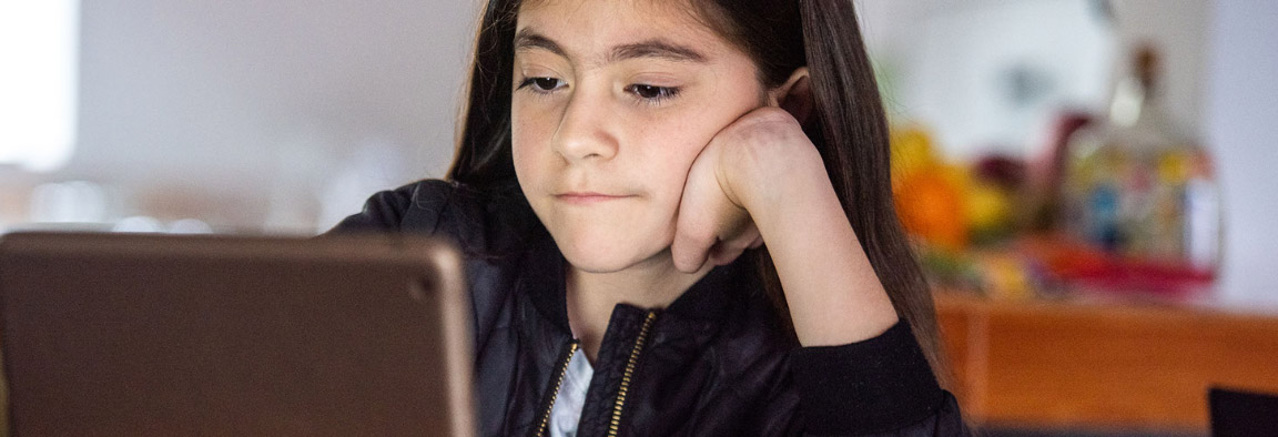 A girl is sitting facing the camera, looking at a tablet screen.